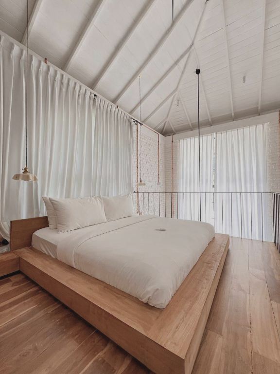 A loft bedroom with a low timber bed beneath a white pitched ceiling